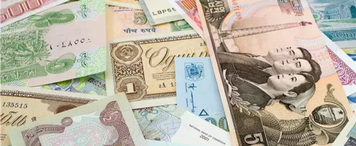 An assortment of currency notes spread out on a table, displaying a variety of colors and denominations from different countries.